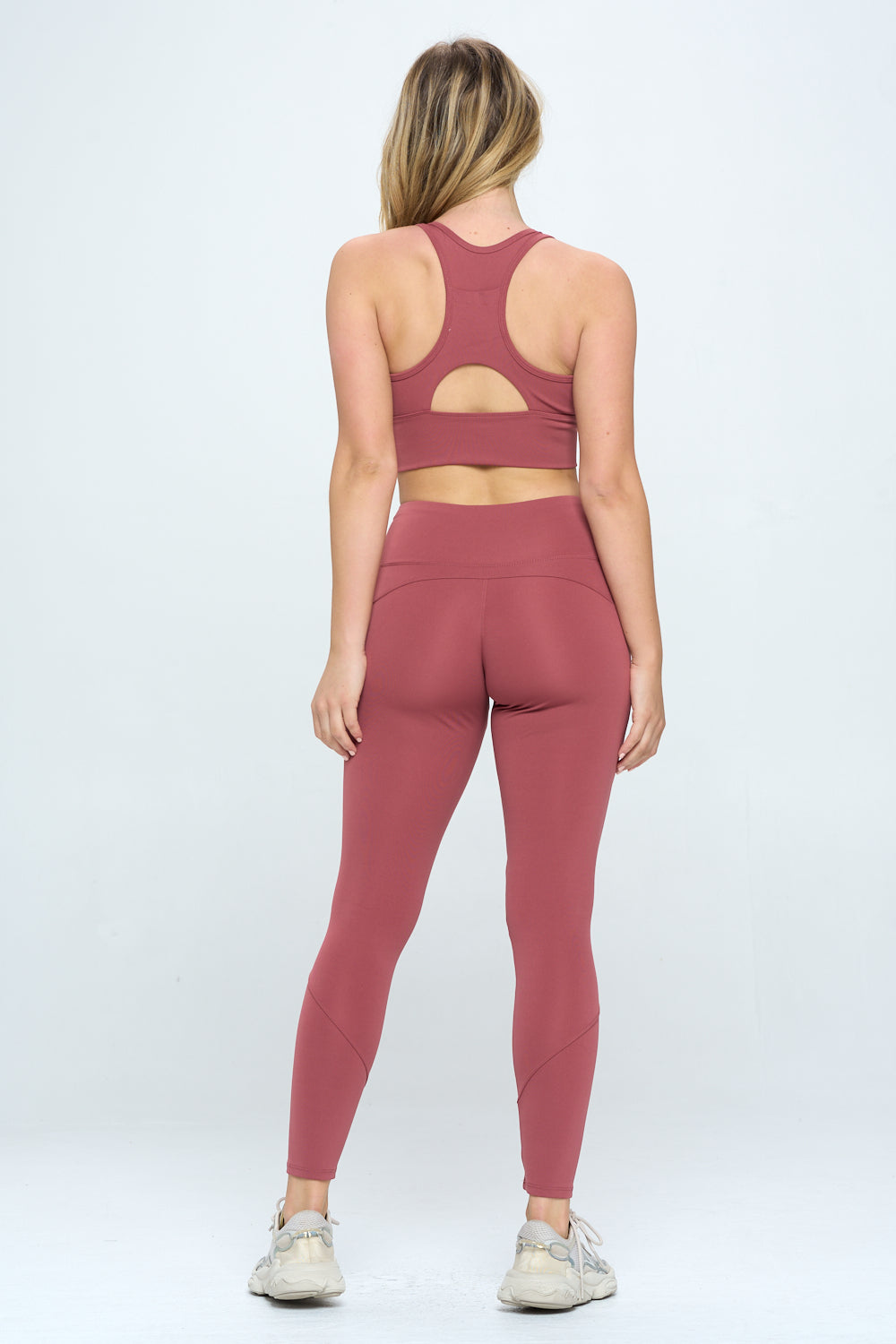 A person with long blonde hair is seen from the back, wearing a matching Harmony Activewear Set of red sports leggings and a sports bra, made from high-stretch fabric. The high-waist outfit is paired with white athletic shoes, set against a plain, light-colored background.