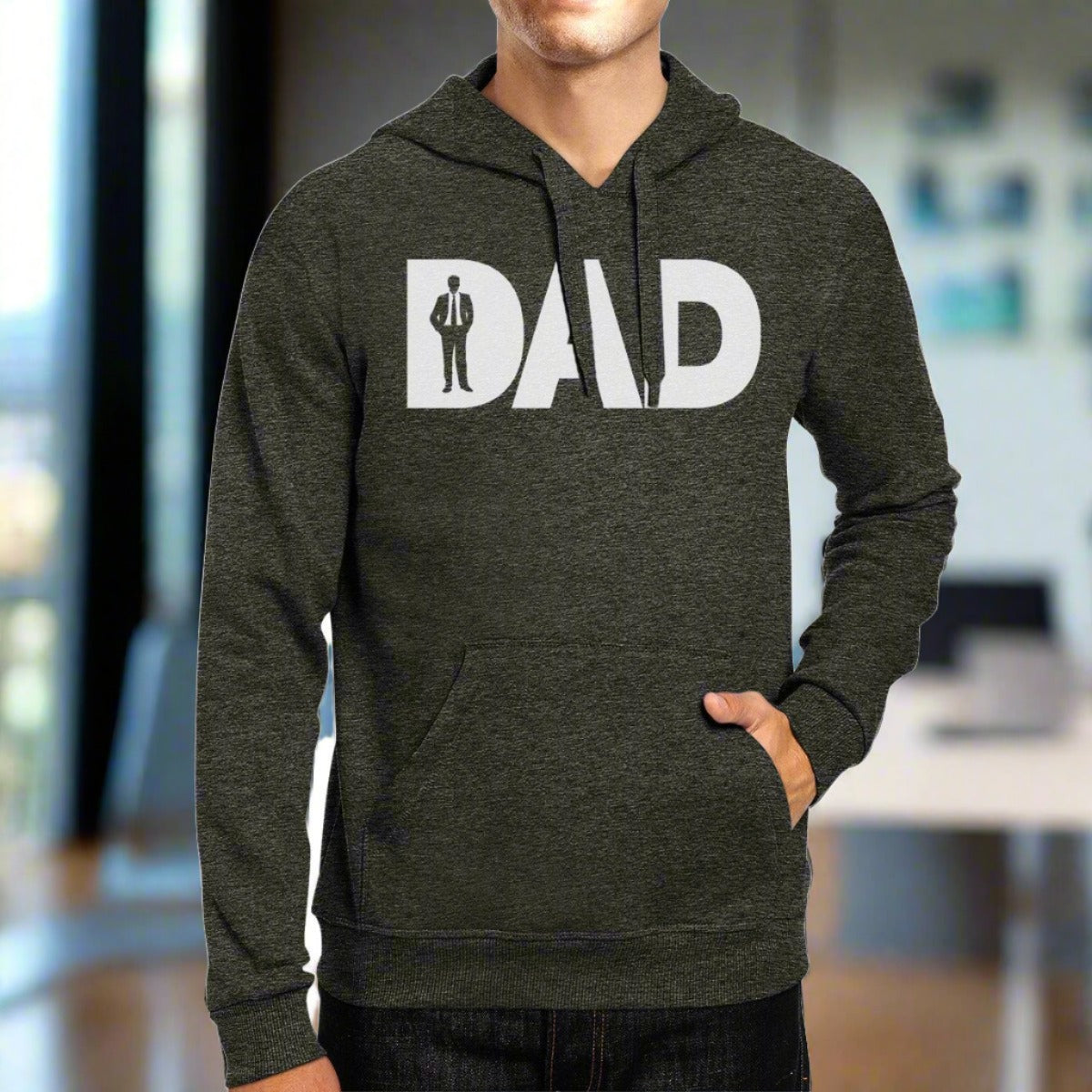 A person wearing a dark grey Working Dad Graphic Hoodie with the word "DAD" printed on it in bold white letters. The letter "A" is stylized to include a silhouette of a working dad in a suit. Perfect for Father’s Day, the person has one hand in the kangaroo pocket of the hoodie.